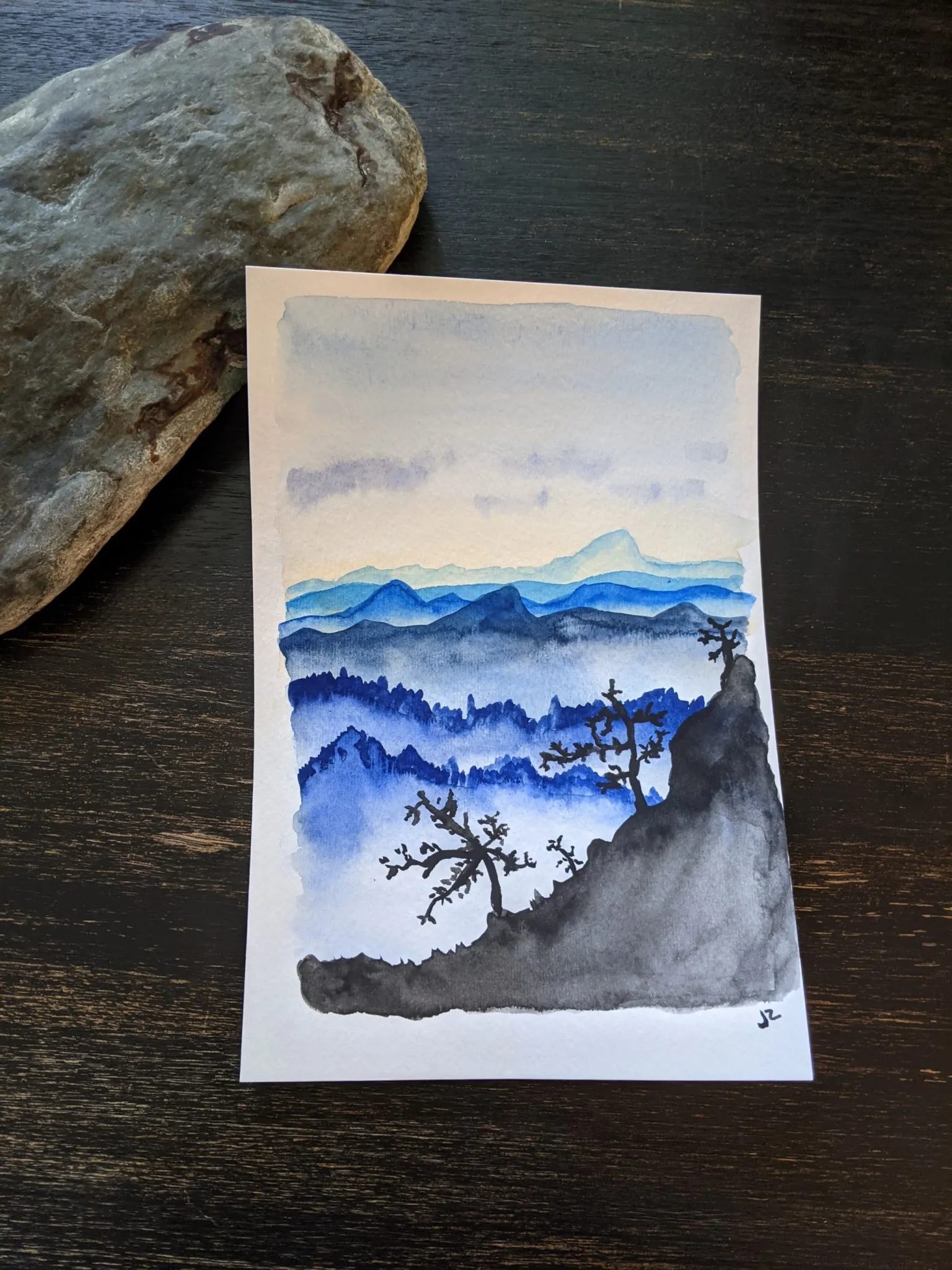 A watercolor painting of blue mountains and a sunrise sky.