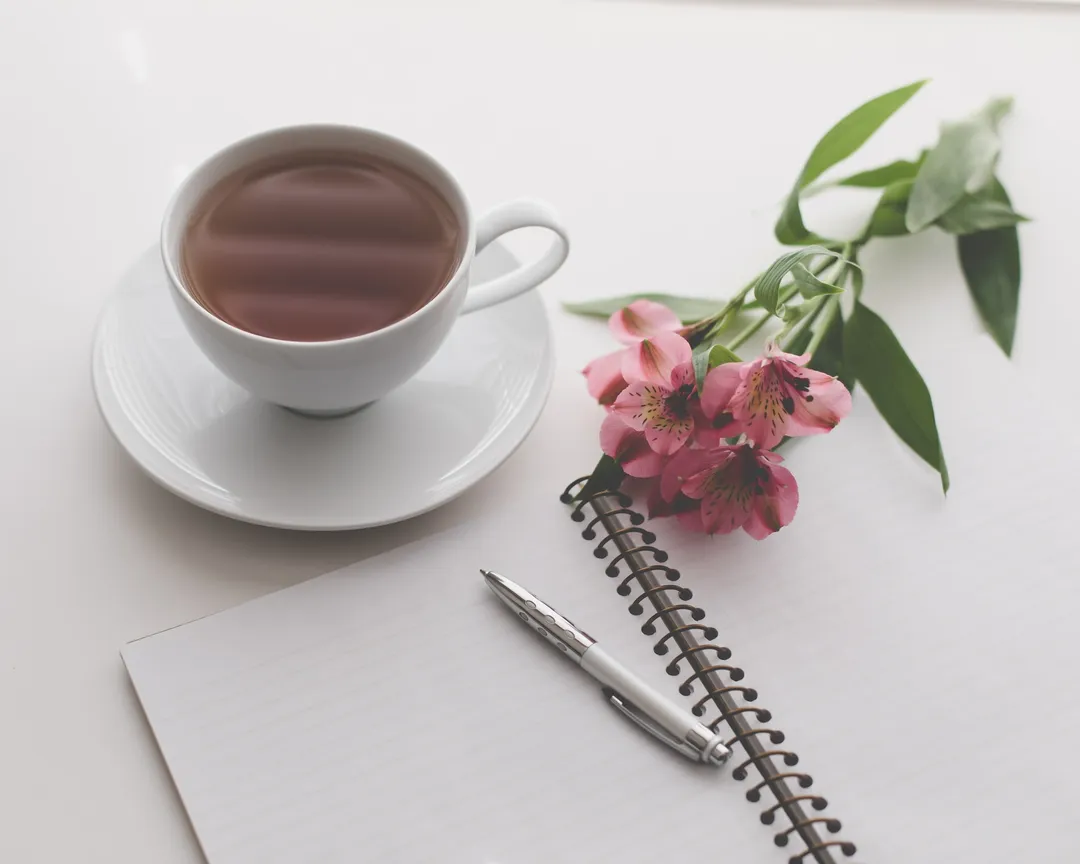 A notebook and a cup of tea on a wooden table.